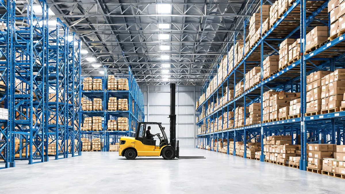 Forklift driving across the concrete floor inside a completed steel warehouse with pallet racking