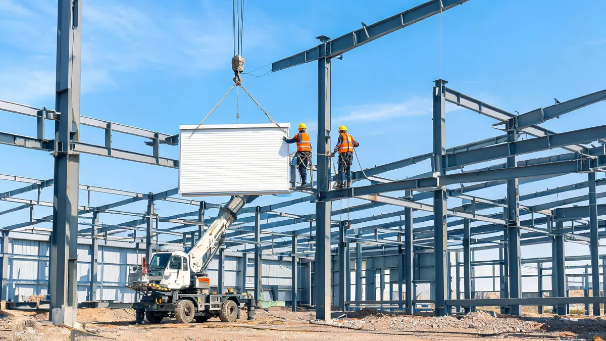 Workers installing insulated sandwich wall panels on a steel frame industrial building