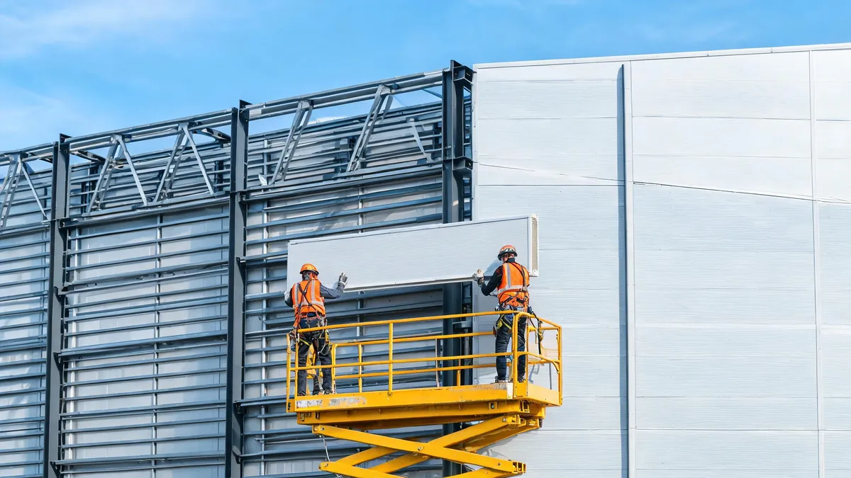Installers fixing insulated sandwich cladding panels to the steel frame wall of a prefabricated warehouse